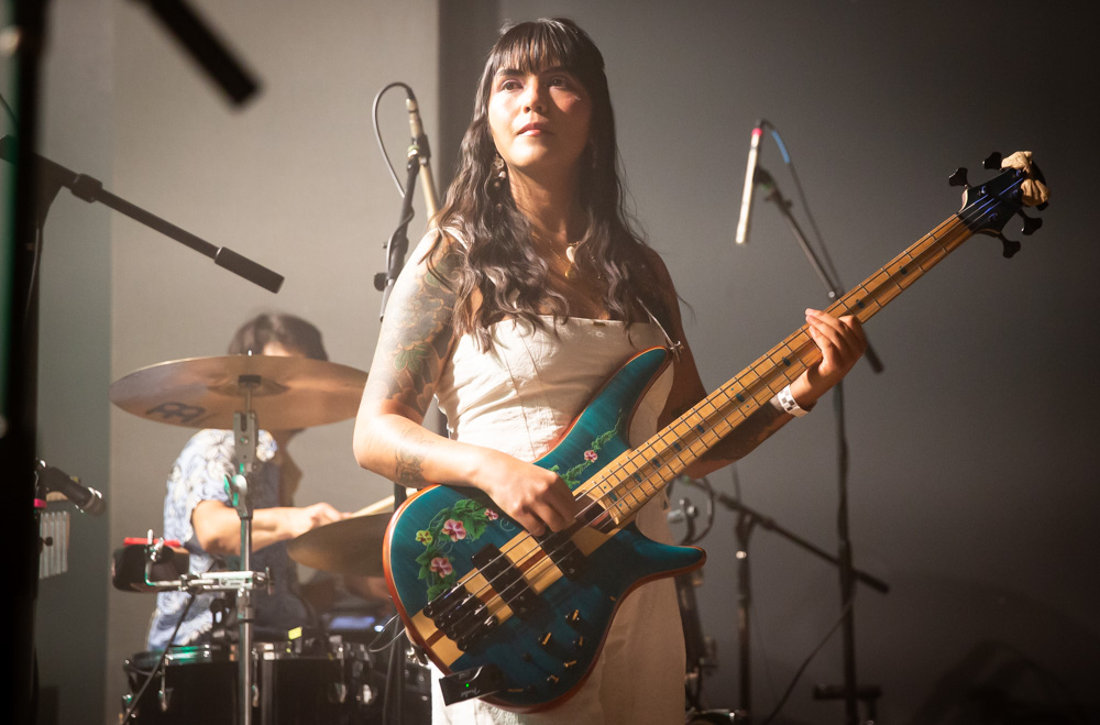 A bassist playing a teal bass with the drummer behind her during BALTHVS at Aisle 5 in Atlanta.