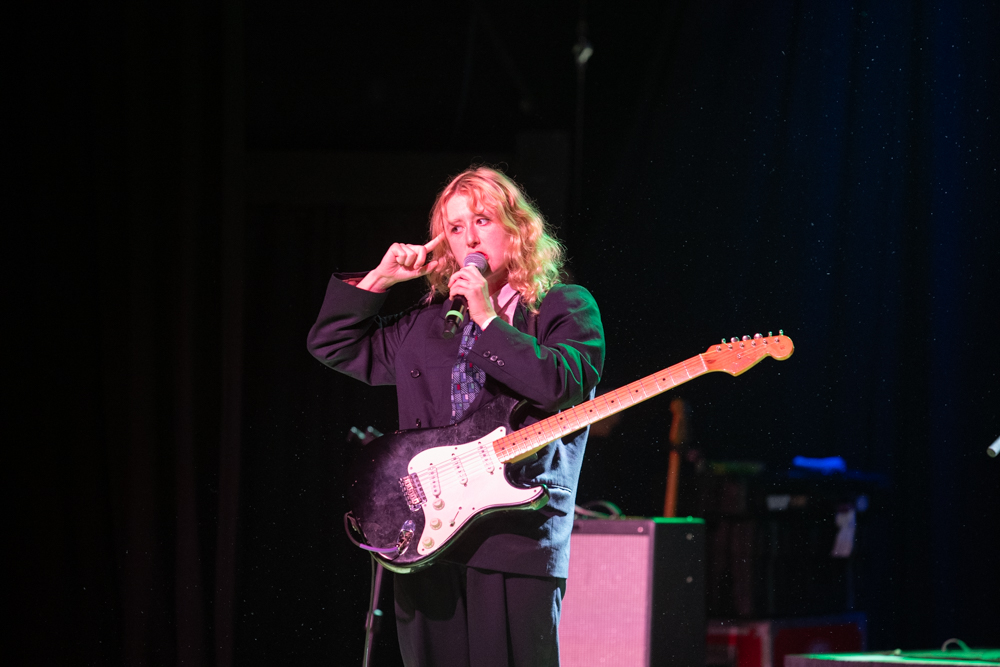 Lambrini Girls vocalist holding a microphone with an electric guitar at Variety Playhouse in Atlanta.